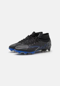 Black soccer cleats with blue accents, textured upper, and a dynamic design. Features a sock-like collar and visible studs for traction.
