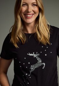 Svart t-shirt med kort ärm som har en silverpaljettrådjursdesign med små stjärnor. Tillverkad av bomull, enkel rund halsringning och klassisk passform.