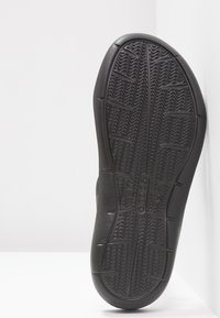 Black rubber shoe sole with a wavy traction pattern. Features a rounded toe and slightly raised edges for durability. Logo visible on the sole.