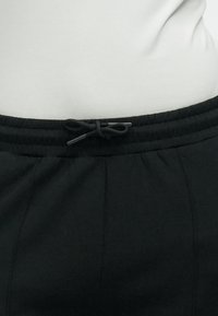 Τα μαύρα παντελόνια φόρμας διαθέτουν ελαστική μέση με κορδόνι, οριζόντιες ραφές και λεία, απαλή υφή.