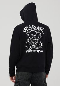 Czarna bluza z kapturem z białym nadrukiem niedźwiedzia z tyłu, z napisem "JESTEM NIEDŹWIEDZIEM ZA KAŻDYM RAZEM," na tle gładkiej tekstury materiału.