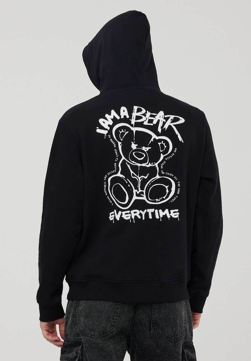 Czarna bluza z kapturem z białym nadrukiem niedźwiedzia z tyłu, z napisem "JESTEM NIEDŹWIEDZIEM ZA KAŻDYM RAZEM," na tle gładkiej tekstury materiału.