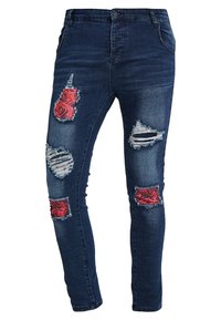 Jeans de denim azul ajustados que presentan parches rasgados con patrones de rosas rojas y detalles desgastados. Cintura estándar con cierre de botón.