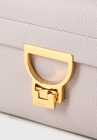 Light pink leather handbag with a textured finish, featuring a gold-tone metal clasp and accent handle, highlighting a sleek, modern design.