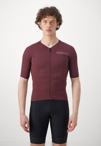 Bordeaux-farbenes, kurzärmeliges Radtrikot mit einem Reißverschluss vorne, das mit einem strukturierten Muster und einem Logodetail versehen ist, kombiniert mit schwarzen Radhosen.