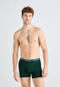 Dunkelgrüne Boxer Shorts aus weichem Material, mit einem einfarbigen Design und einem kontrastierenden weißen Logo-Bund. Glatte Textur, figurbetonte Passform.
