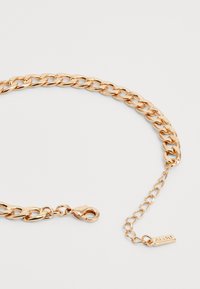 Gold-toned metal chain with wide links, featuring a lobster clasp and an adjustable extension chain with a tag accent. Smooth texture.