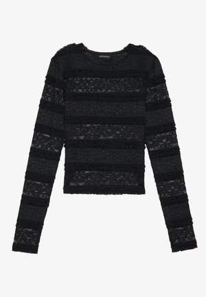 Svart langermet genser med et teksturert, stripete blonderdesign. Har volanger på kantene og en rund halslinning.