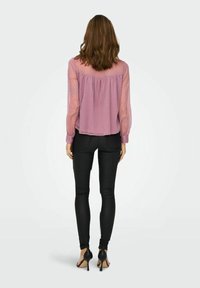 Blouse rose pâle à manches transparentes et dos froncé, associée à un pantalon skinny noir et des chaussures à talons noires. Texture lisse dans l'ensemble.