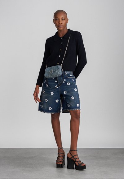 Mørk ribbestrikket cardigan med krage, kombinert med denimshorts med hvit blomsterbroderi, og svarte stroppekilesandaler.