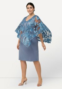 Blå klänning i ett slätt tyg, med en genomskinlig spetsöverdrag med blommig broderi och breda ärmar. Accentuerad med öppna tåskor.