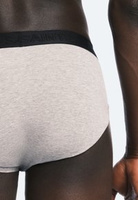 Caleçons en coton gris avec une taille noire arborant un logo en relief. Le tissu a une texture lisse et un design ajusté.