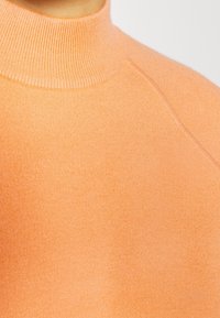 Jersey de cuello alto de color naranja claro, de punto, con un cuello acanalado y una textura suave, con mangas raglán y un diseño minimalista.
