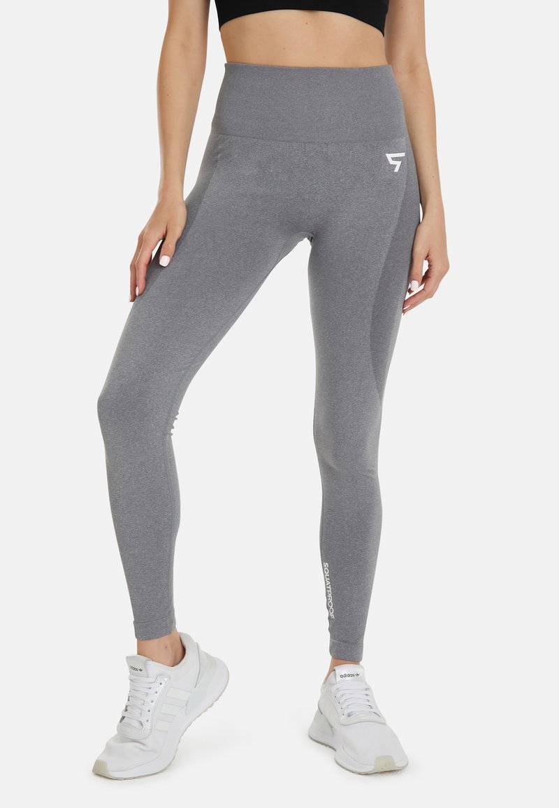 Grijze high-waisted leggings met een gladde textuur, voorzien van een zijlogo en een aansluitend ontwerp, gecombineerd met witte sportschoenen.