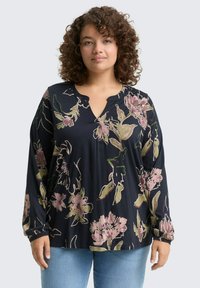 Blouse longue bleu marine foncé à manches longues avec un col en V, des motifs floraux en rose et vert, et une coupe décontractée. Tissu doux et texturé.