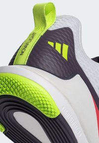 Chaussure de course légère avec une tige texturée blanche et violette, des accents néon verts audacieux, et une semelle à motifs dotée de caractéristiques de traction.
