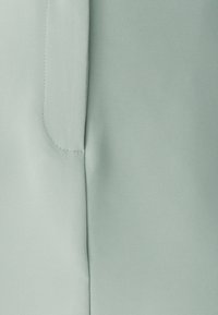 Tessuto verde chiaro con una superficie liscia. Presenta una cucitura e un minimo dettaglio di cucitura. Nessun motivo o accento visibile.