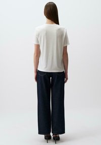T-shirt bianco a maniche corte abbinato a jeans a gamba larga blu scuro a vita alta. L'outfit presenta un design semplice con una vestibilità comoda.