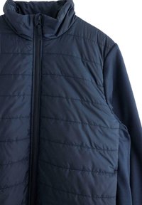 Gilet imbottito blu navy con collo alto, cuciture orizzontali trapuntate, zip frontale completa e pannelli in tessuto morbido ai lati.