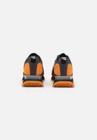 Scarpe sportive nere e arancioni realizzate in materiali mesh e sintetici, con una suola imbottita e accenti riflettenti sul tallone.