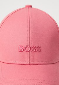 Casquette de baseball rose en tissu avec des coutures brodées, présentant un logo "BOSS" en relief sur le panneau avant.