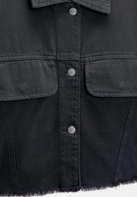 Czarna kurtka dżinsowa z dwoma kieszeniami na piersi z patką, srebrnymi zatrzaskami, postrzępionym dołem i usztywnionym kołnierzem.