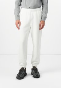 Witte sweatpants met een elastische tailleband, taps toelopende boorden en een zachte textuur, gecombineerd met zwarte sneakers met een mesh-ontwerp en veters.