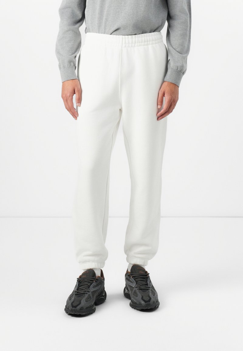Witte sweatpants met een elastische tailleband, taps toelopende boorden en een zachte textuur, gecombineerd met zwarte sneakers met een mesh-ontwerp en veters.