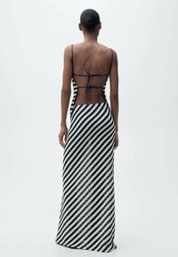 Sort og hvid stribet maxi-kjole med fitted bodice, gennemsigtig ryg, justerbare stropper og en flydende nederdel med diagonale linjer.
