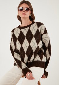 Brah in krem pulover z argyle vzorcem, ohlapnega kroja, z ribanim izrezom in manšetami, izdelan iz mehke, teksturirane tkanine.