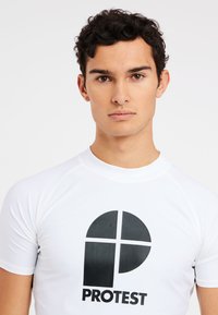 Witte rash guard met korte mouwen, voorzien van een opvallend zwart "PROTEST" logo en een cirkelvormig grafisch ontwerp aan de voorkant.