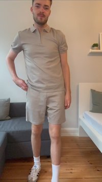 Svijetlosmeđi polo majica s dizajnom polu-rajnglja, u kombinaciji s odgovarajućim šortsevima. Model stoji u ležernim cipelama na neutralnoj pozadini.