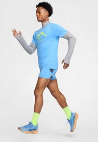 Helles blaues Sportshirt mit grauen langen Ärmeln, blaue Shorts mit geteilter Design, und neongrüne Socken, kombiniert mit blauen Laufschuhen.