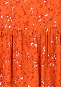 Oranssi kangas kukkakuviolla, jossa on pieniä valkoisia ja vaaleanpunaisia kukkia. Materiaali on sileä, ja helmassa on rypytetty yksityiskohta.