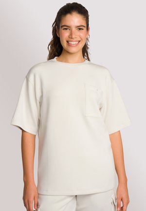 Helles beiges Oversized-T-Shirt mit Rundhalsausschnitt, kurzen Ärmeln und einer Brusttasche. Hergestellt aus weich-natürlichem, glattem Material.