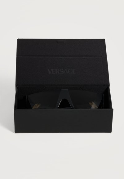 Lunettes de soleil noires Versace avec des verres foncés partiellement visibles à l'intérieur d'une boîte noire ouverte avec le logo Versace sur le couvercle intérieur.