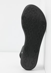 Semelle de sandale en caoutchouc noir avec des motifs texturés, informations de taille embossées et une forme lisse et contourée pour le confort et le soutien.