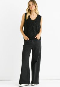 Black sleeveless top with a V-neck, adorned with small sparkles. Paired with high-waisted wide-leg black jeans and silver shoes.