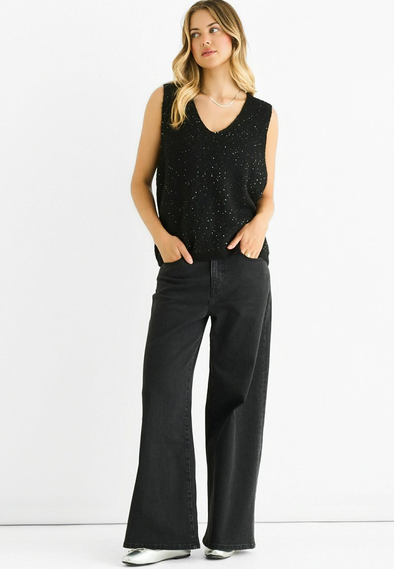 Black sleeveless top with a V-neck, adorned with small sparkles. Paired with high-waisted wide-leg black jeans and silver shoes.