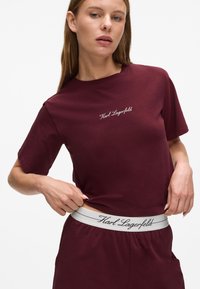Bordeaux katoenen t-shirt met korte mouwen, voorzien van geborduurd "Karl Lagerfeld" logo. Draagt met bijpassende bordeaux pantalon en elastische tailleband.