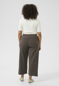 Brown wide-leg pants with an elastic waistband, made of lightweight fabric. Paired with a white fitted top and beige slip-on shoes.