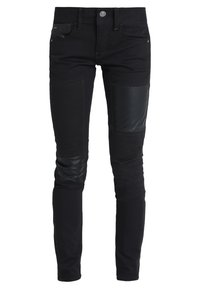 Black slim-fit jeans with reinforced matte black patch on right thigh and textured patch on left knee, featuring front button and pockets.