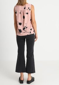 Vaaleanpunainen hihaton paita mustalla kukkakuviolla, ryhdistetty takapuoli, yhdistetty istuviin mustiin liehuviin farkkuihin ja mustiin korokepohjakenkiin.