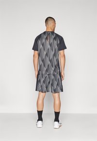 Mannelijke sportoutfit bestaande uit een shirt met korte mouwen en shorts in het zwart met een geometrisch patroon en een oranje accent bij de halslijn.