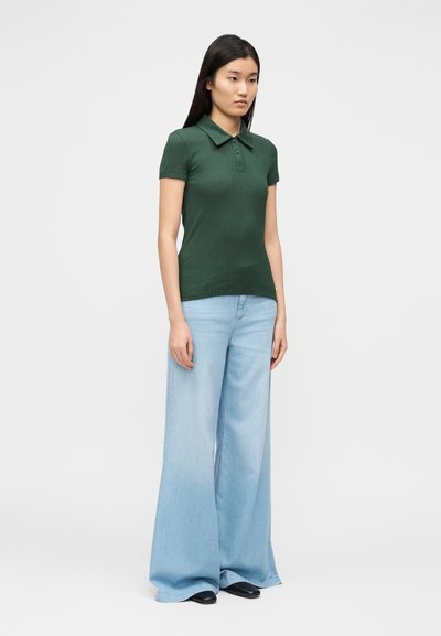 Πράσινο πόλο με ρίγες, γιακά και τρία κουμπιά, σε συνδυασμό με φαρδιά τζιν παντελόνια σε ανοιχτό μπλε χρώμα. Μαύρα παπούτσια ολοκληρώνουν το σύνολο.