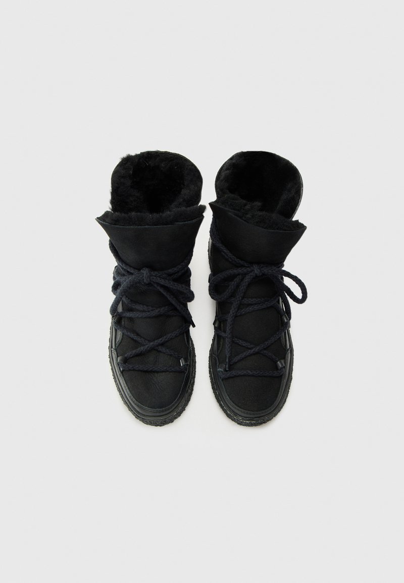 Czarne ocieplone buty mają teksturowaną skórzaną powierzchnię, grube czarne sznurowadła oraz miękką futrzaną podszewkę, z możliwością złożenia cholewy dla regulacji.