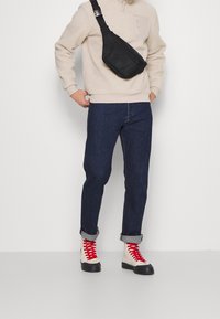 Sudadera de forro polar beige, vaqueros de mezclilla oscuros, zapatillas altas negras y rojas. Bandolera negra con detalle de cremallera. Puños enrollados en los vaqueros.