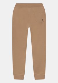 Hnědé tepláky s hladkou texturou, přiléhavými manžetami, elastickým pasem a jednou zadní kapsou s malým logem.