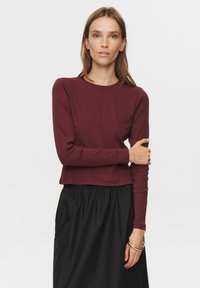 Burgunderfarbendes Langarmoberteil mit Rundhalsausschnitt, weichem Material und figurbetontem Schnitt, kombiniert mit einem schwarzen, gerafften Rock. Einfacher und lässiger Look.