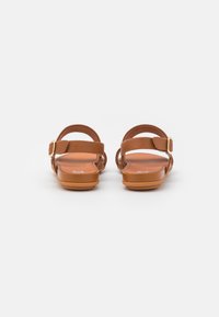 Bruine leren sandalen met platte zolen, verstelbare gespen en open achterkant. Glad textuur met een minimalistisch ontwerp.